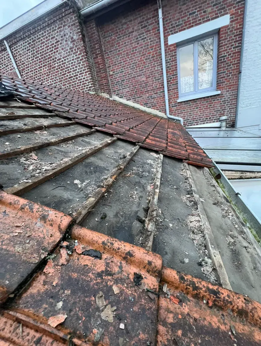 Ancienne couverture usée, tuiles cassées et plaques abîmées, au pied d’un mur en briques