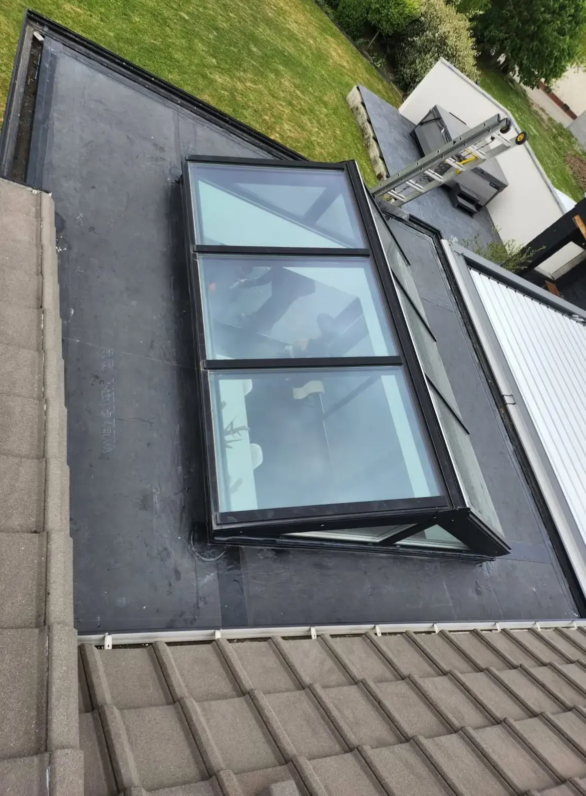 Verrière posée sur un toit plat, au-dessus d’une toiture en tuiles